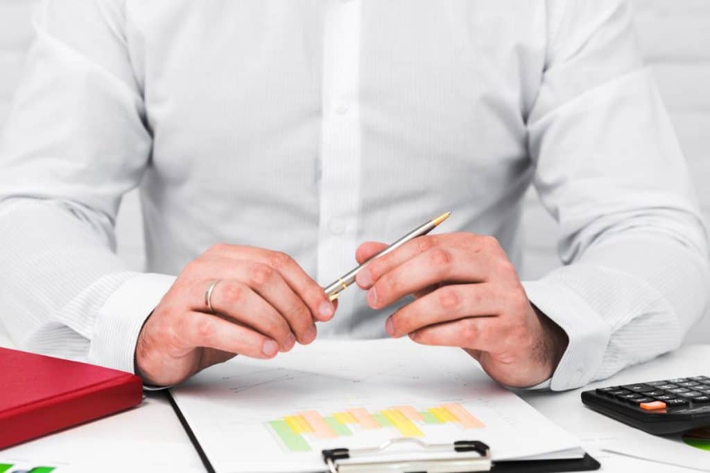 - פרסום ישראל Person in a white shirt holds a pen over documents on a desk, with a red binder and a calculator nearby