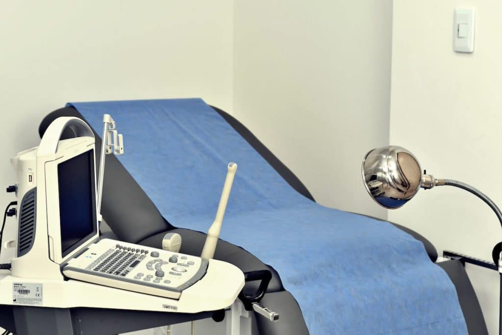 - פרסום ישראל Ultrasound machine and examination table covered with blue sheet in a medical room ready for a patient.