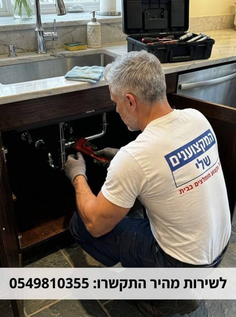- פרסום ישראל Plumber kneeling under a kitchen sink, using a wrench with an open tool case nearby